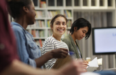 Young woman sitting and smiling while talking to her peers during a seminar