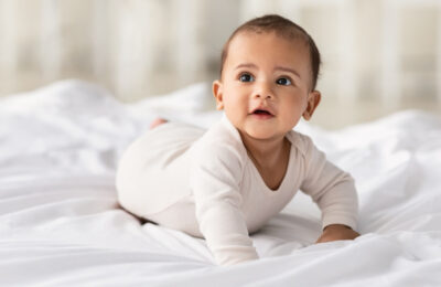 Portrait of cute little baby wearing bodysuit lying on white bedsheets