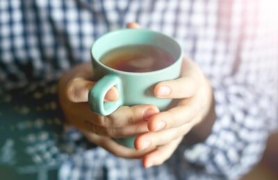 Hands around a green mug of steaming tea