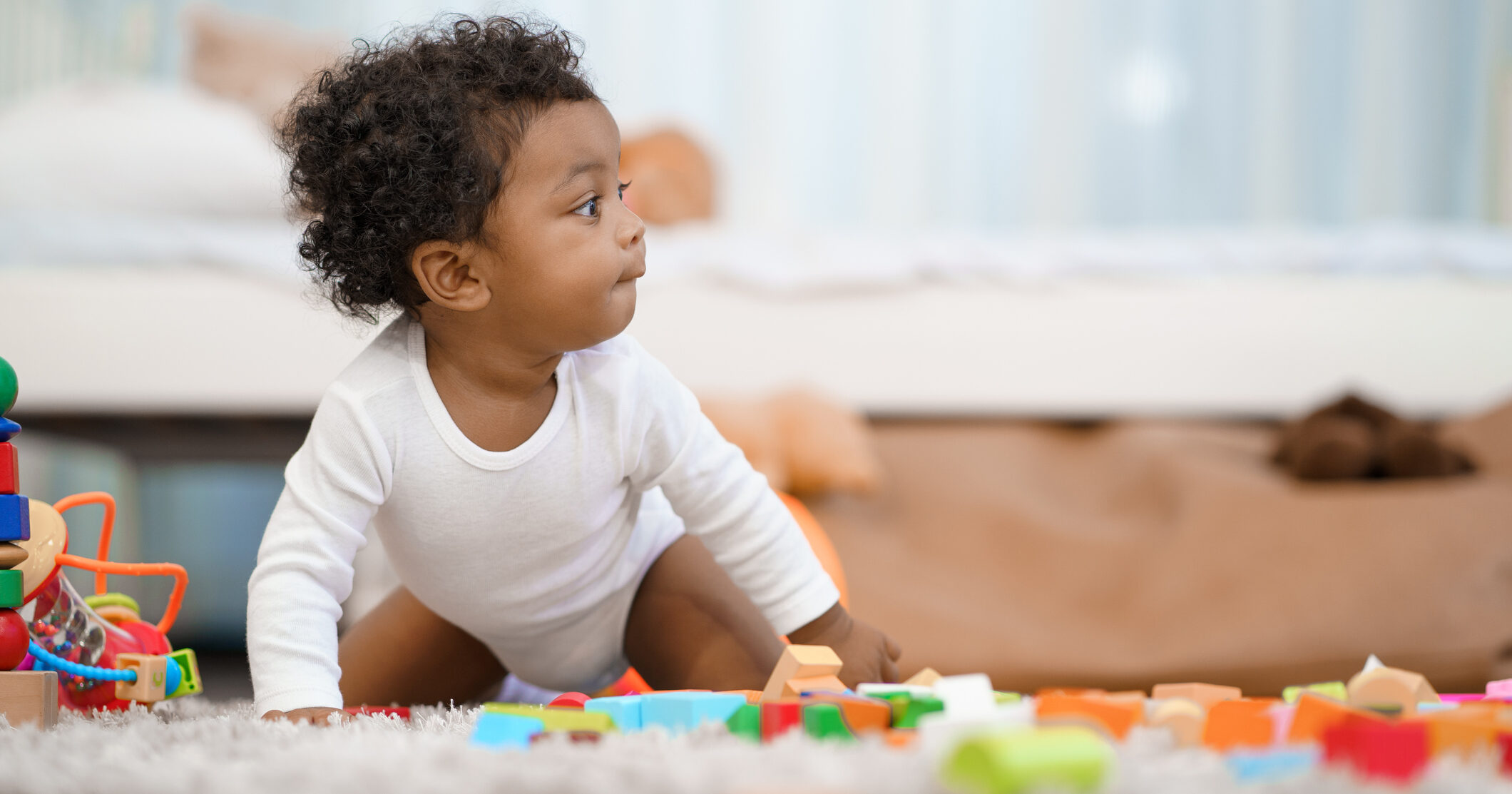 Infant crawling amongst toys in bedroom