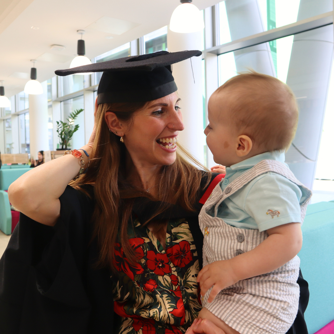 A female graduate holding a baby. 