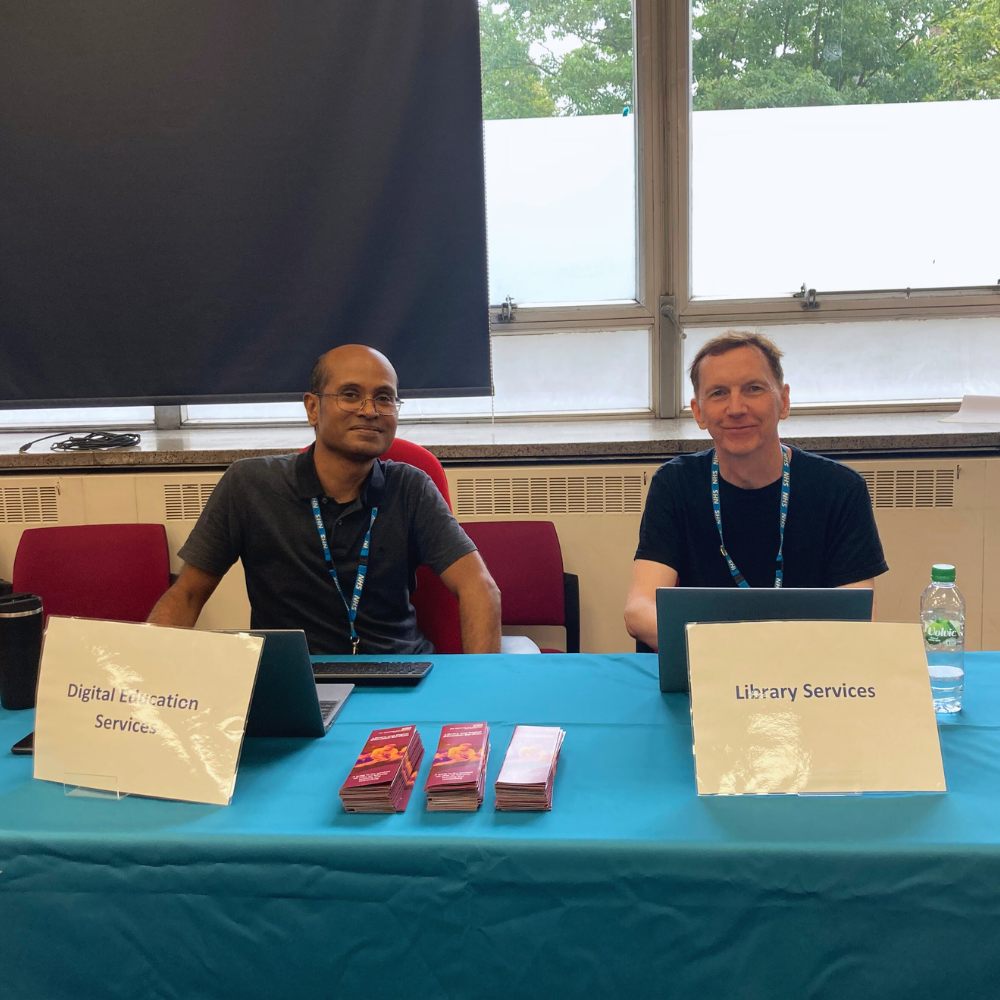 Two men sitting at a table to welcome new students to the Library. 