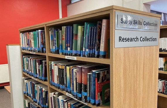 The image shows a wooden bookshelf filled with various books and study materials organized on its shelves. There are two signs: one saying "Study Skills Collection" and the bottom is "Research Collection".