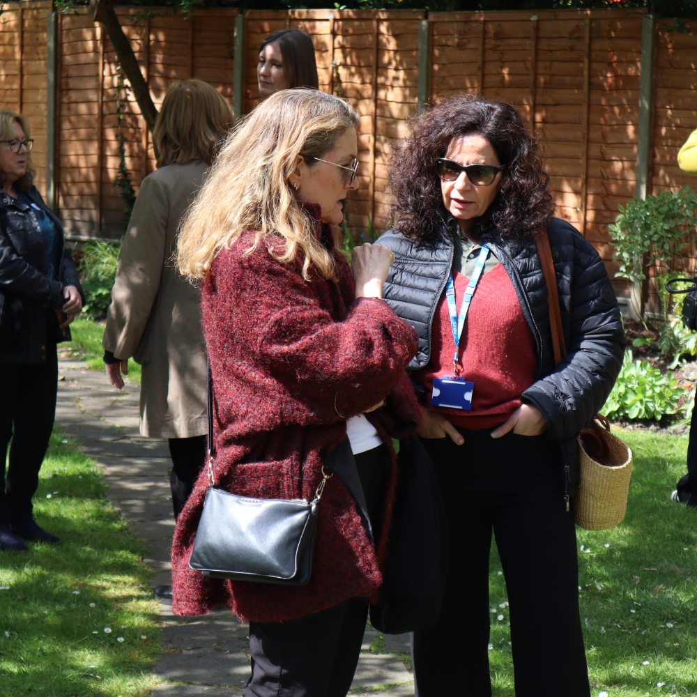 Two people chatting in the Tavistock garden, with a group of people behind them.