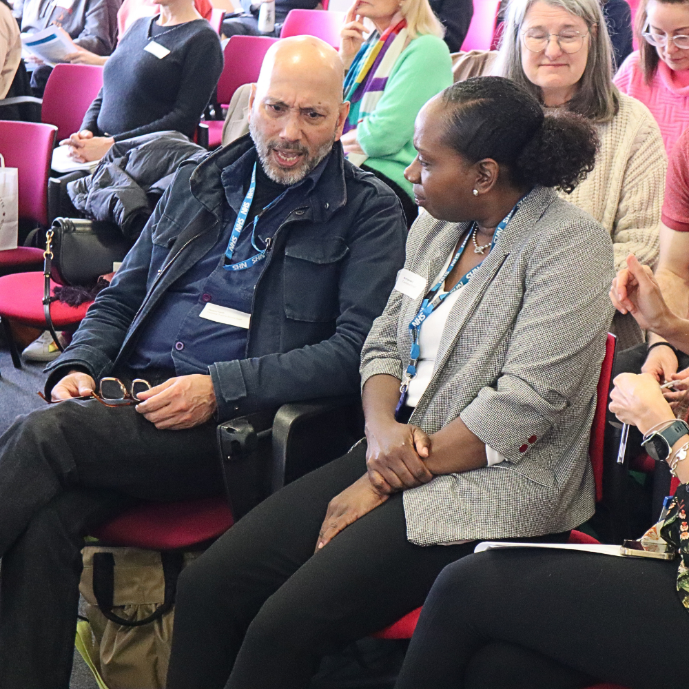 Two members of the audience chatting in the lecture theatre at the Tavistock Centre.