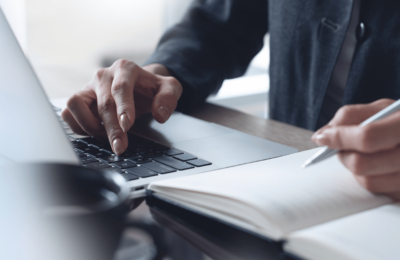 Close-up of a person's hands working with a keyboard and notebook.