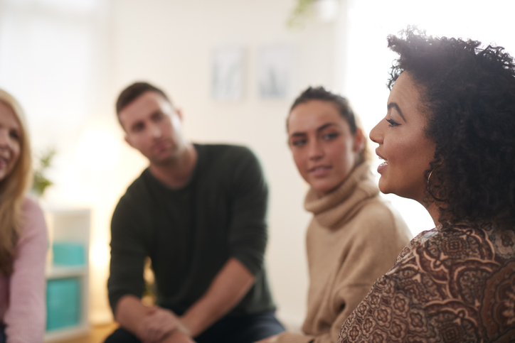 Women talking with peers who are sat in a semi-circle with their heads turned in and listening