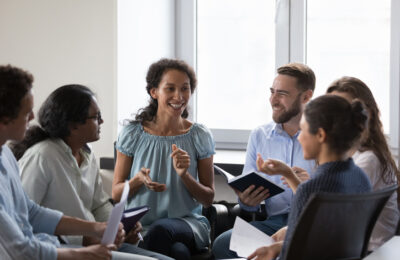 A group of colleagues at work who are sat on chairs in a circle discussing work