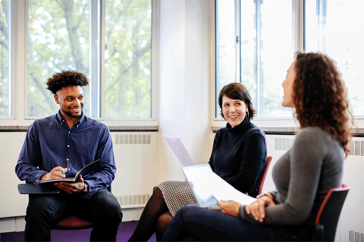 Teacher and two students sat on read chairs in a semi circle with windows behind them