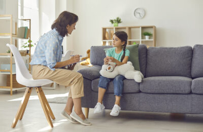 Professional female child psychologist working with a little preschool girl in a bright office. Woman makes notes about the condition of the girl on paper. Children's mental therapy.