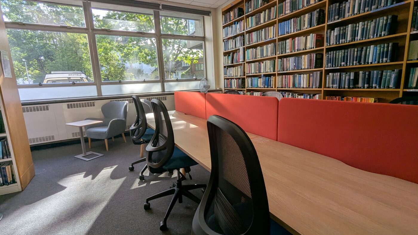 The Tavistock Centre library silent study space with a row of study desks with chairs, and a book shelf