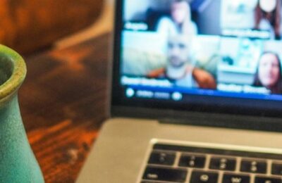 A laptop shows a zoom event with multiple callers. There is a green ceramic mug next to the laptop.