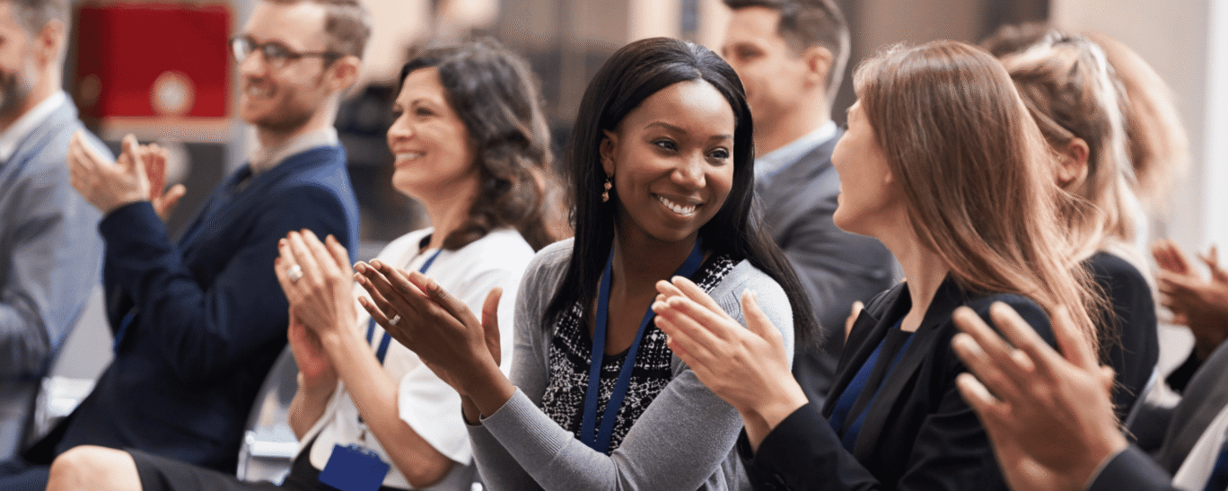 Audience smile and applaud at conference.
